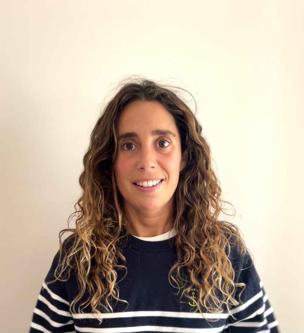 Maria smiling, wearing a navy striped sweater, in front of a cream wall